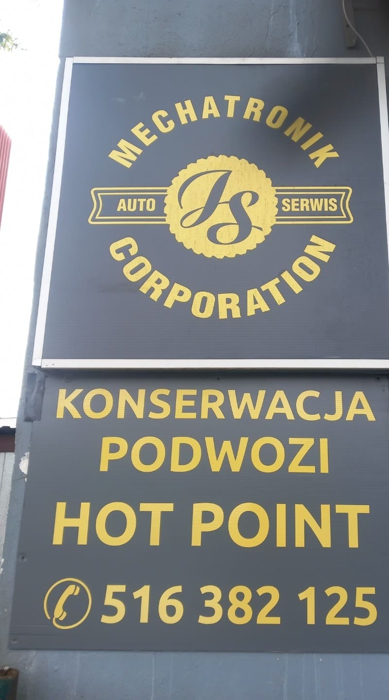 Szyld przy wjeździe do warsztatu z logo Mechatronik oraz napisem konserwacja podwozi, Hot Point, numer telefonu 516 382 125.