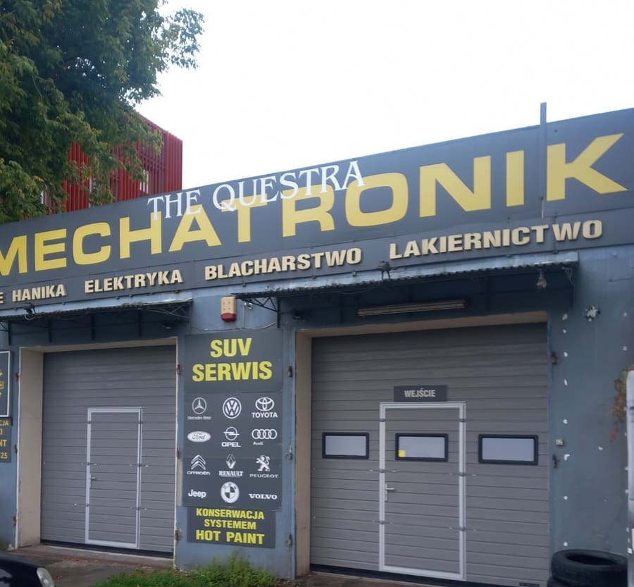 Tablica przy wjeździe do warsztatu Mechatronik z napisem SUV SERWIS i logotypami obsługiwanych marek: Mercedes-Benz, Volkswagen, Toyota, Ford, Opel, Audi, Citroën, Renault, Peugeot, Jeep, BMW, Volvo, oraz informacją o konserwacji systemem Hot Paint.