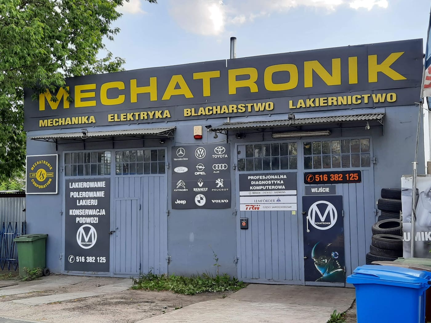 Front warsztatu Mechatronik przy ul. Glinki w Bydgoszczy: żółty szyld z napisem MECHATRONIK i podpisem mechanika, elektryka, blacharstwo, lakiernictwo, dwie bramy warsztatowe i wejście z okrągłym logo warsztatu.